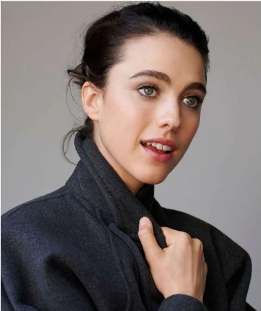 A close-up studio portrait captures a woman with fair skin and dark hair, wearing a charcoal gray coat. She is looking off-camera.