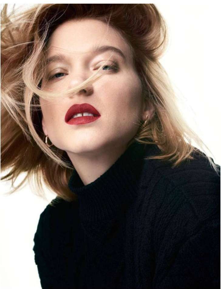 Close-up studio portrait of a young adult woman with blonde wavy hair and red lipstick wearing a black turtleneck sweater.
