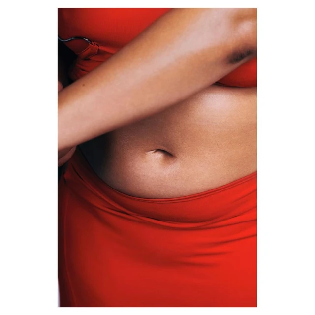 Close-up shot of a fair-skinned female torso wearing a red skirt and bra top, emphasizing skin texture and shape against a plain background.
