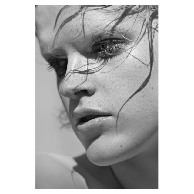 Black and white close-up portrait of a woman with freckles and wet hair, looking down in an outdoor setting, with soft lighting.