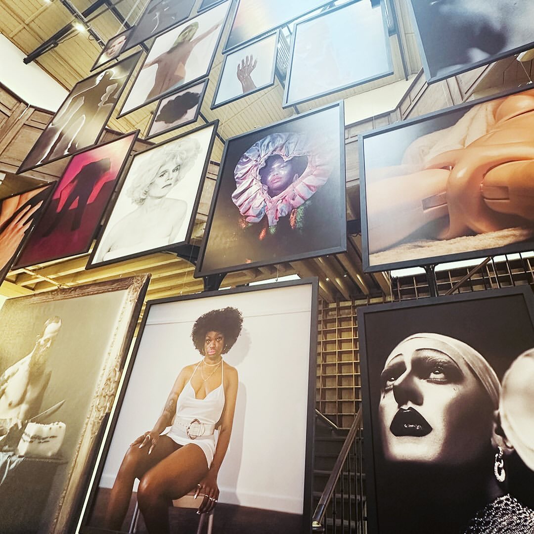 Art gallery installation with multiple framed photos of diverse people hanging from the ceiling on display in an indoor setting.