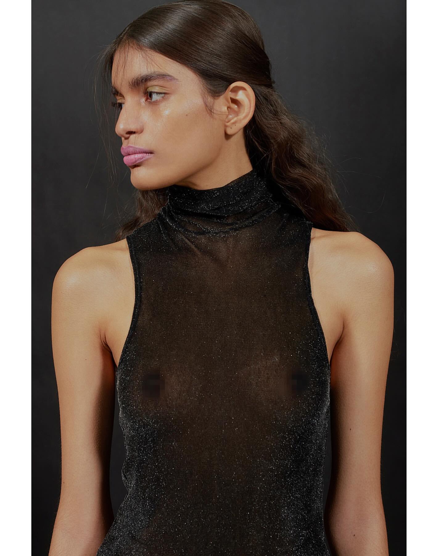 Elegant portrait of a young woman with soft pink lips and dark hair posing in a dark shimmering high-neck top against a dark background.