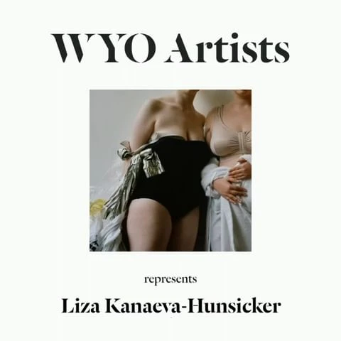 Two women pose indoors, one in black swimwear with a metallic shawl and the other in a light-colored dress, in a studio-lit fashion shot.