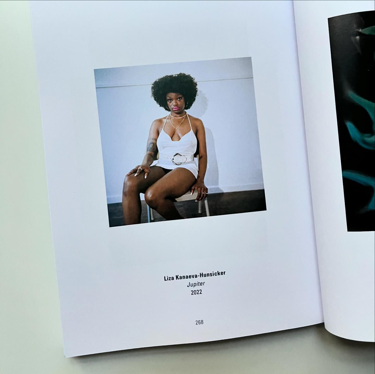 Photo in an open book of a woman sitting on a chair wearing a white outfit with a white wall in the background.
