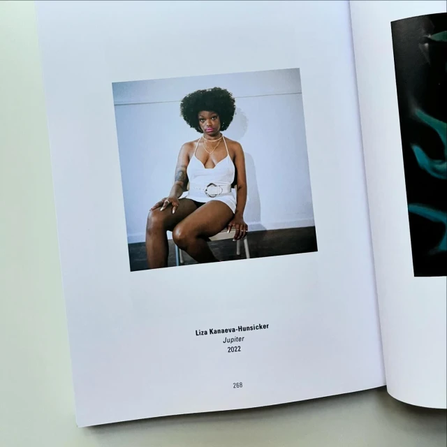Photo in an open book of a woman sitting on a chair wearing a white outfit with a white wall in the background.
