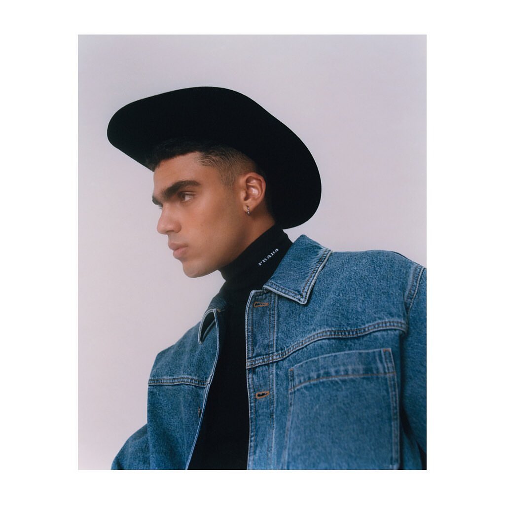 Portrait of a male model in a black cowboy hat and denim jacket, set against a neutral background in a studio setting.