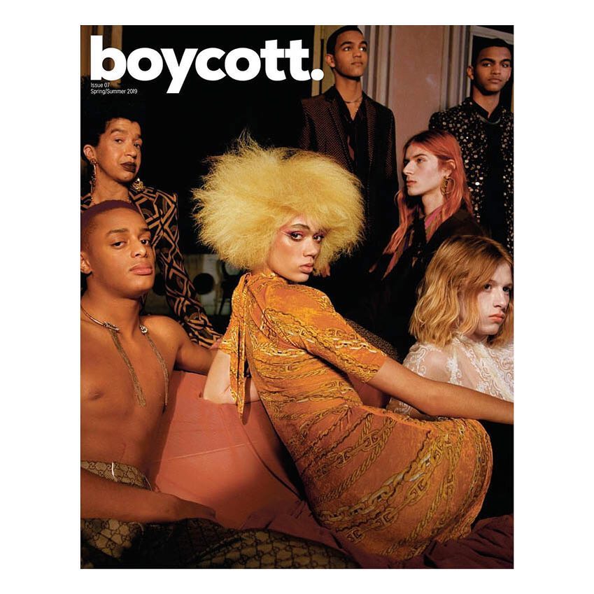 Fashion magazine cover featuring seven diverse models in stylish clothing and makeup, set against a dark background with bright lighting.