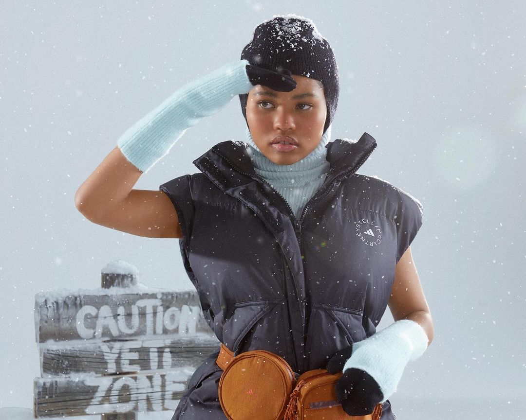 A young woman in winter apparel shields her eyes, standing outside in a snowy setting with a 'Caution Yeti Zone' sign.