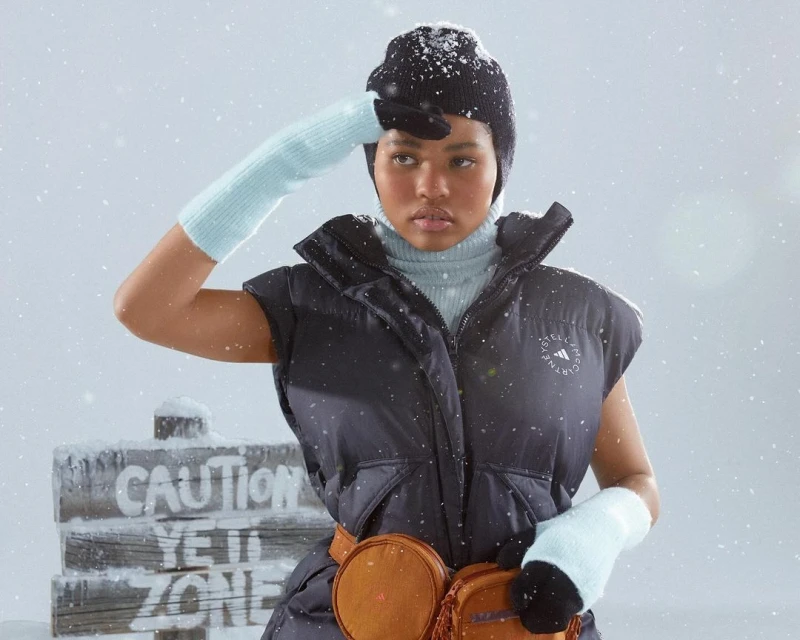 A young woman in winter apparel shields her eyes, standing outside in a snowy setting with a 'Caution Yeti Zone' sign.