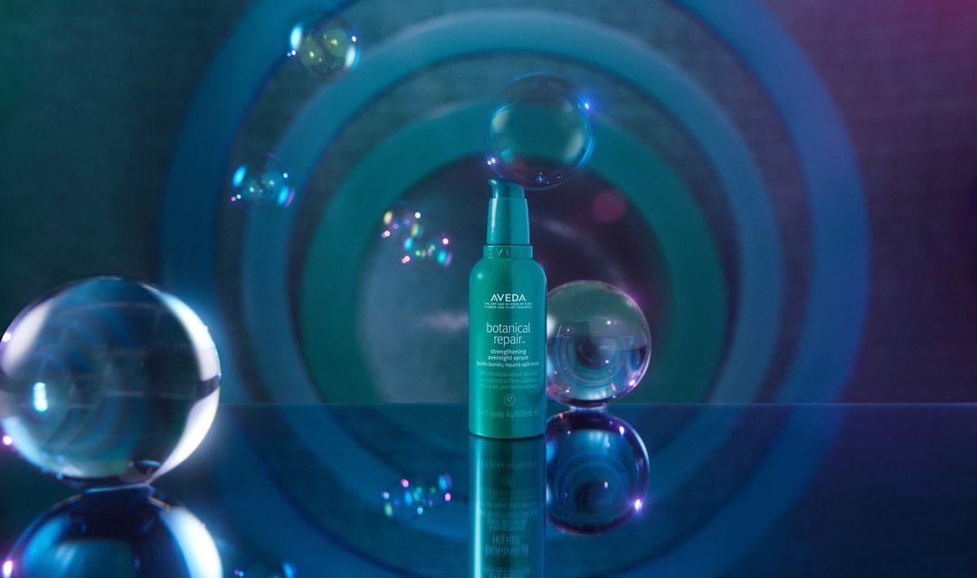 Aveda Botanical Repair strengthening overnight serum bottle with clear spheres, set against a gradient blue and purple background.