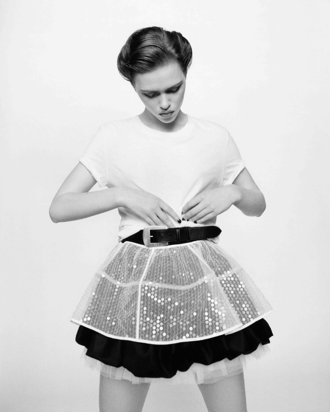 Model in white t-shirt and layered skirt adjusting belt against white background