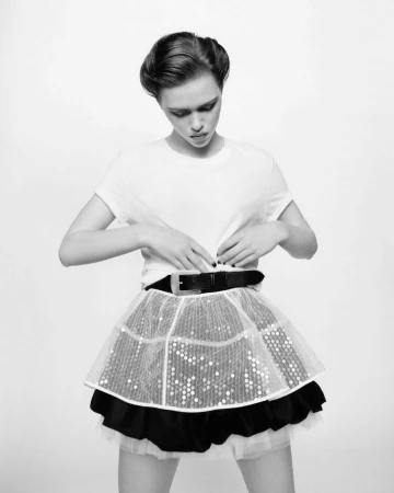 Model in white t-shirt and layered skirt adjusting belt against white background