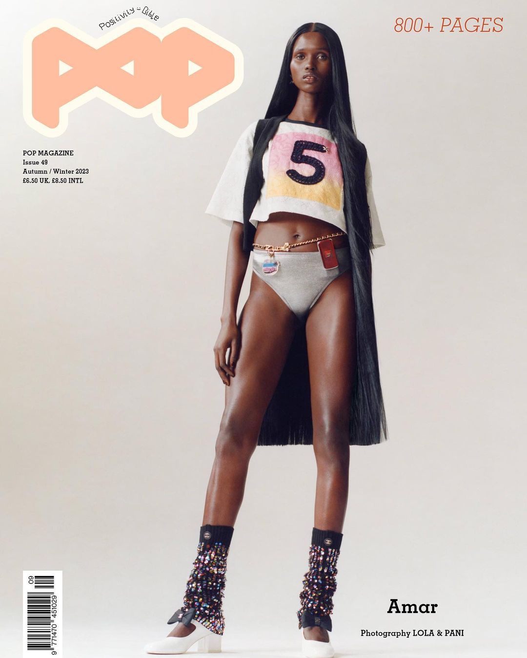Fashion magazine cover featuring a slender woman in a crop top and briefs, accessorized with leg warmers and a necklace belt, posing on white.