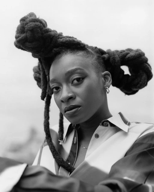 Black and white portrait of an adult female with a serious facial expression, wearing a button-down shirt, and unique, styled dreadlocks.