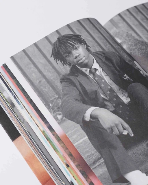 Monochrome portrait of a teenage male in school uniform, seated on a set of book pages, black and white rendering on a white background.