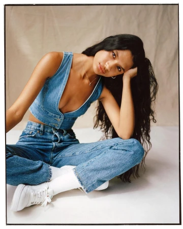 Young woman in denim vest and jeans seated on the floor against a textured backdrop by photographers Lola and Pani