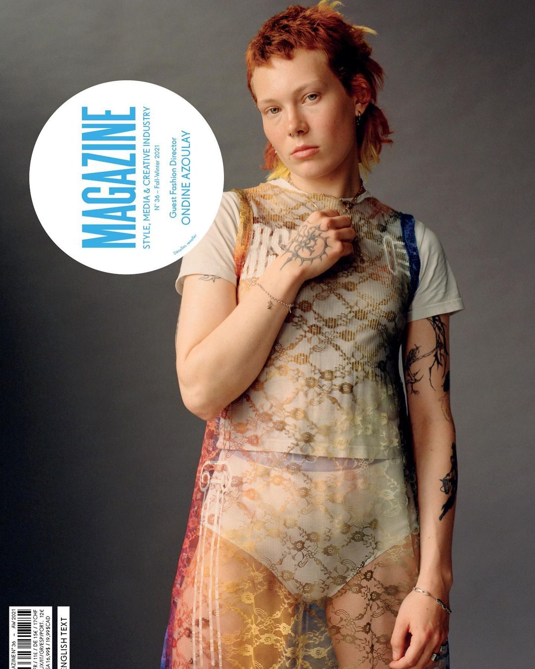 Magazine cover featuring a red-haired person with tattoos wearing a sheer patterned top and briefs against a gray backdrop.