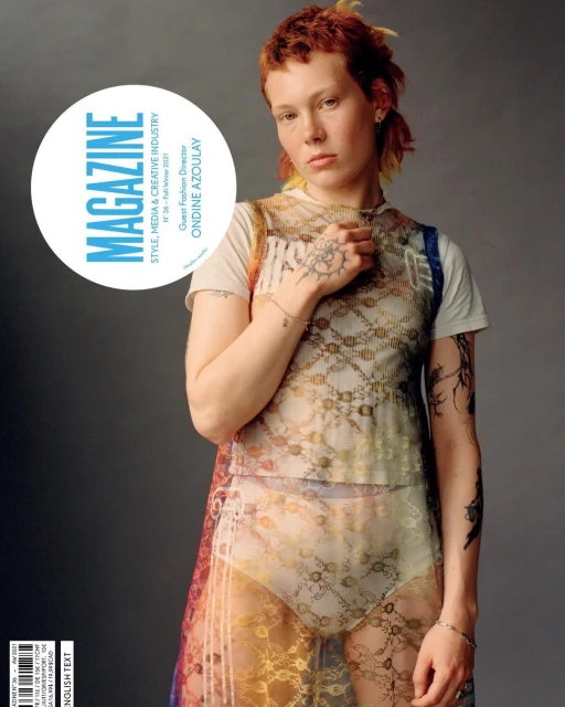 Magazine cover featuring a red-haired person with tattoos wearing a sheer patterned top and briefs against a gray backdrop.