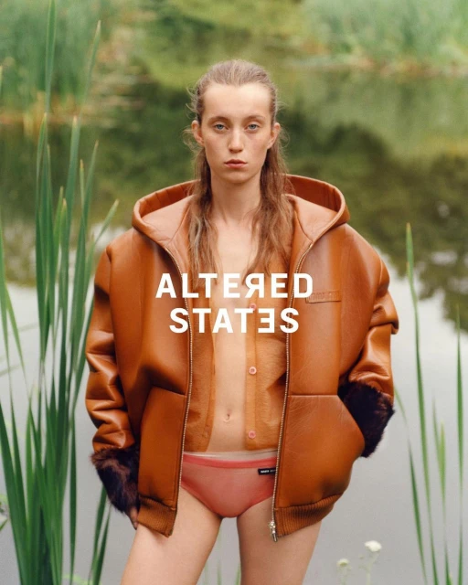A model wears an oversized brown leather hooded jacket and coral underwear in front of a reedy pond, with text overlay.