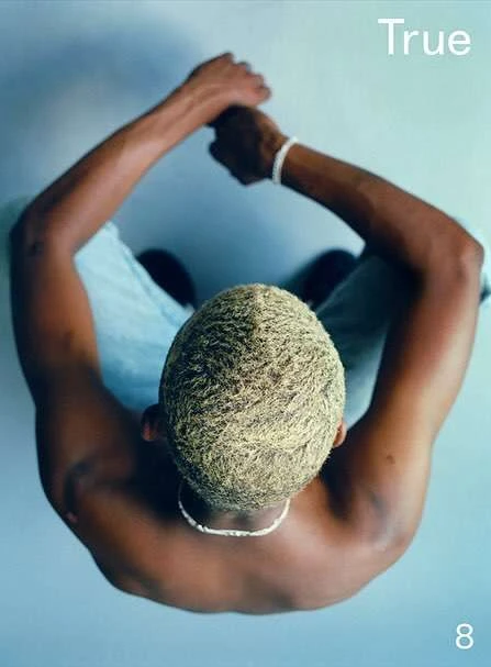 Overhead shot of a dark-skinned man with blonde hair and casual attire, creating a serene and stylish visual composition indoors.