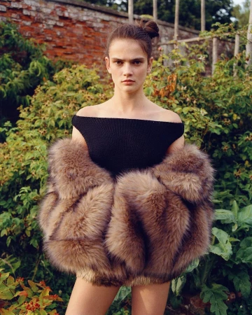 Model in an off-the-shoulder black top wearing a fluffy brown fur jacket outdoors in a garden by Lola and Pani