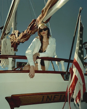 Woman wearing sunglasses and headscarf leaning on a boat railing with an American flag