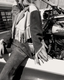 Model wearing fringe suede jacket sitting on vintage pickup truck next to motorcycle by Lorenzo Cisi