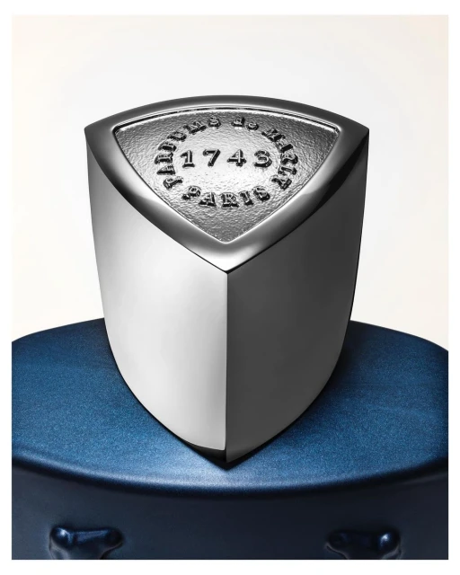 Close-up studio shot of a metallic and blue perfume bottle, featuring embossed text on a shield-shaped emblem. Luxury fragrance product.