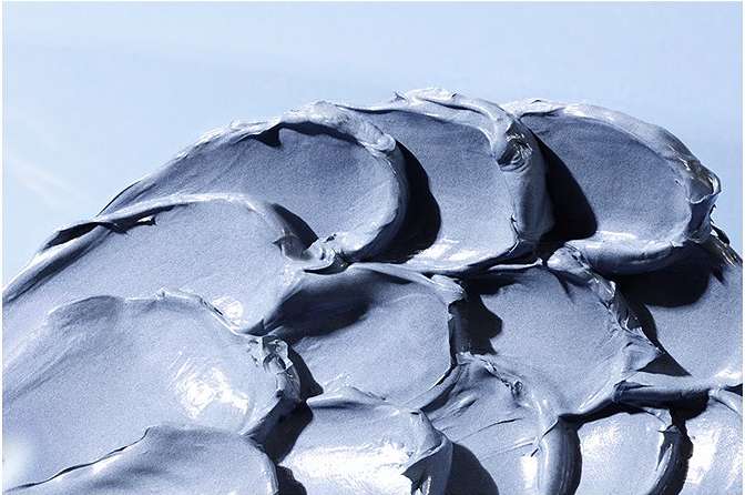 Close-up of a thick, swirled layer of pale blue cosmetic cream against a light blue background, highlighting its texture and consistency.