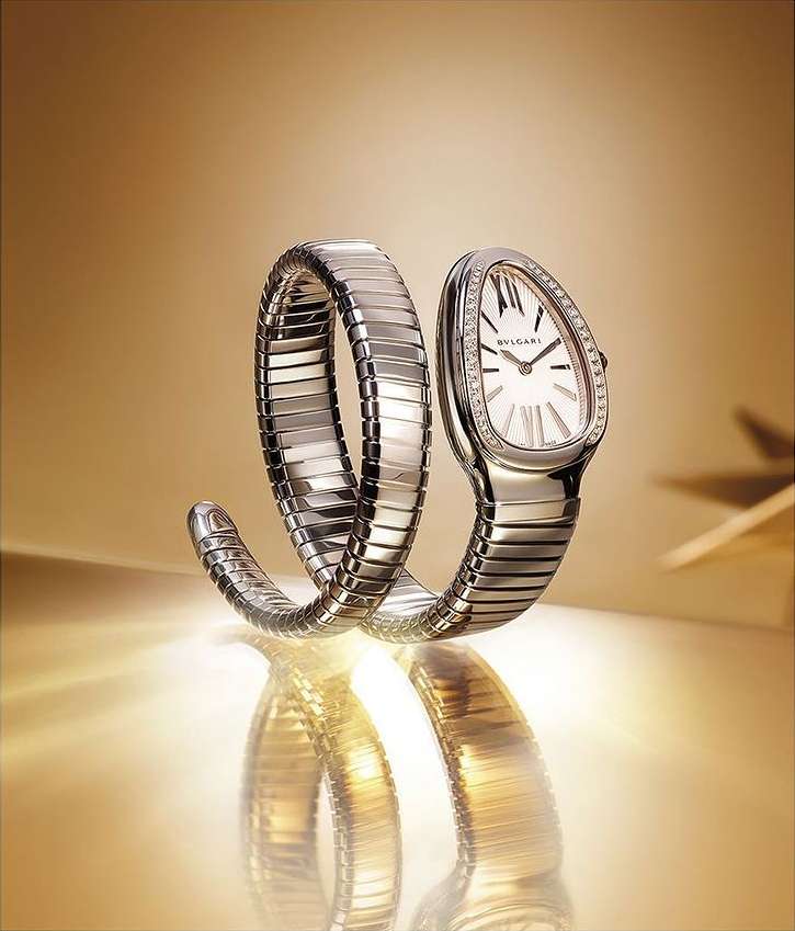 Serpenti Seduttori watch by Bulgari with a silver flexible bracelet and a white dial, displayed on a shiny gold surface.