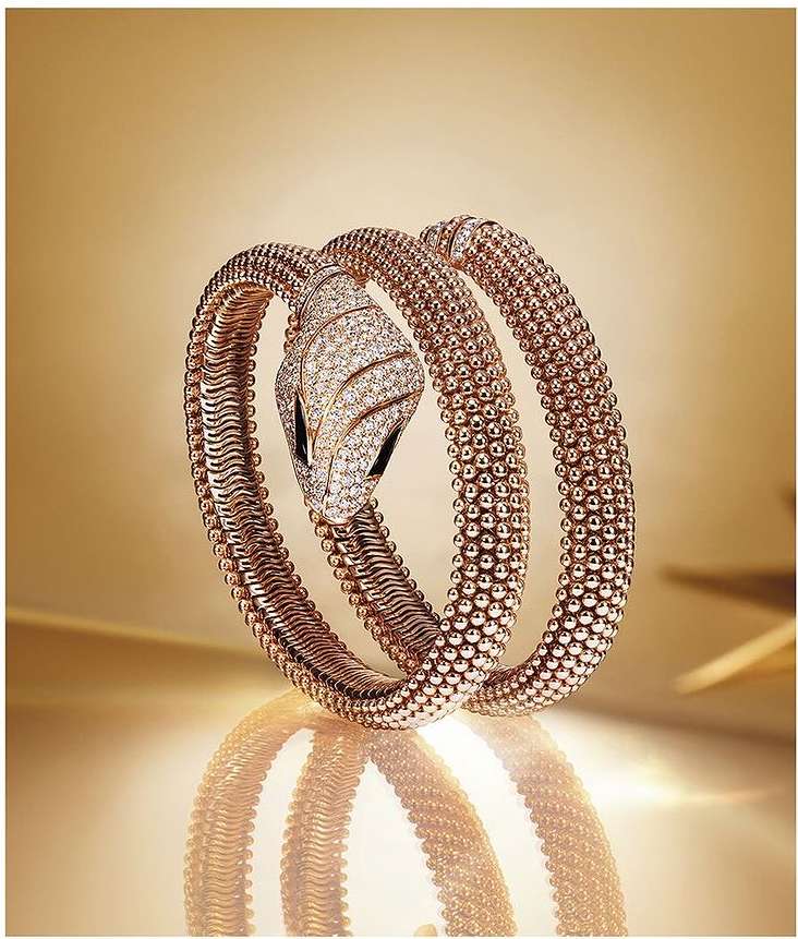 Snake bracelet in rose gold with diamonds set against a warm golden background with a reflective surface.