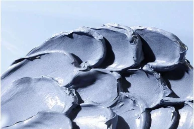 Macro view of smooth grey cosmetic cream swatches with visible peaks and ridges against a pale blue background.