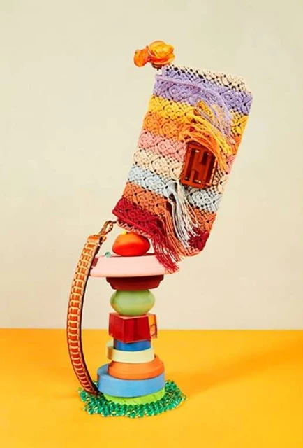 Crochet handbag with a flower accent, presented atop a colorful tower of assorted shapes against a cream and yellow background.