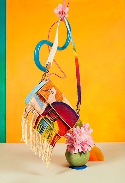 Stylized handbag with fringe, embroidery, and graphic art hangs with colorful decoration, flowers, and an orange and yellow background.
