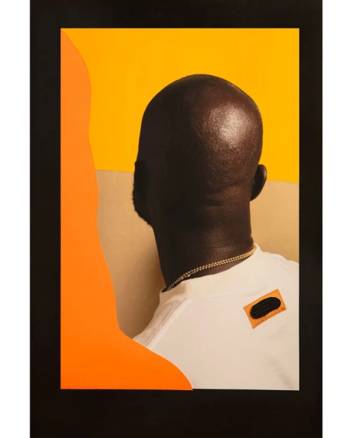 Portrait of a bald black man facing away wearing a white t-shirt and gold chain against a two-tone yellow and beige background.