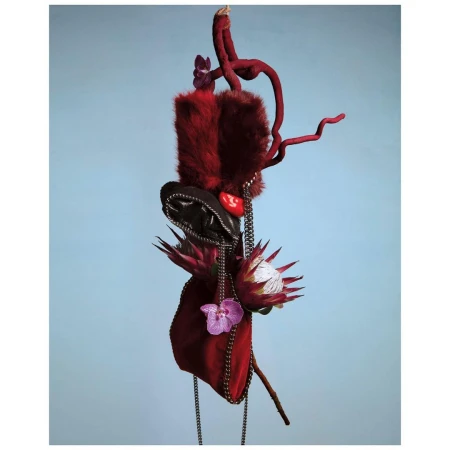 Sculptural artwork featuring red fur, flowers, and metallic chains against a plain pale blue background