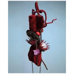 Sculptural artwork featuring red fur, flowers, and metallic chains against a plain pale blue background