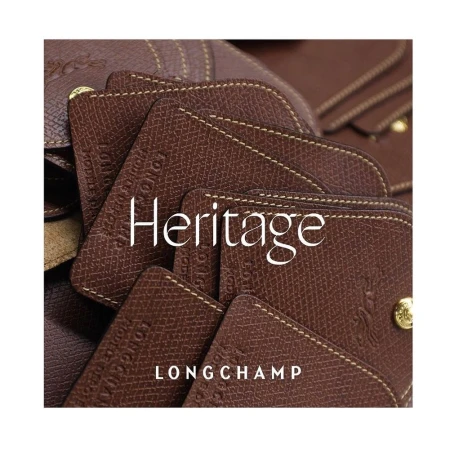 Close-up on the Longchamp Heritage leather goods collection featuring a brown leather flap bag with a gold snap closure and visible stitching.