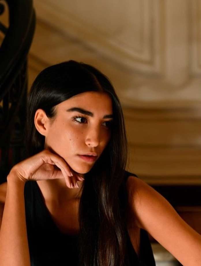 Portrait of a woman with long dark hair wearing a black sleeveless top, resting chin on hand in Paris by Lou Levy.