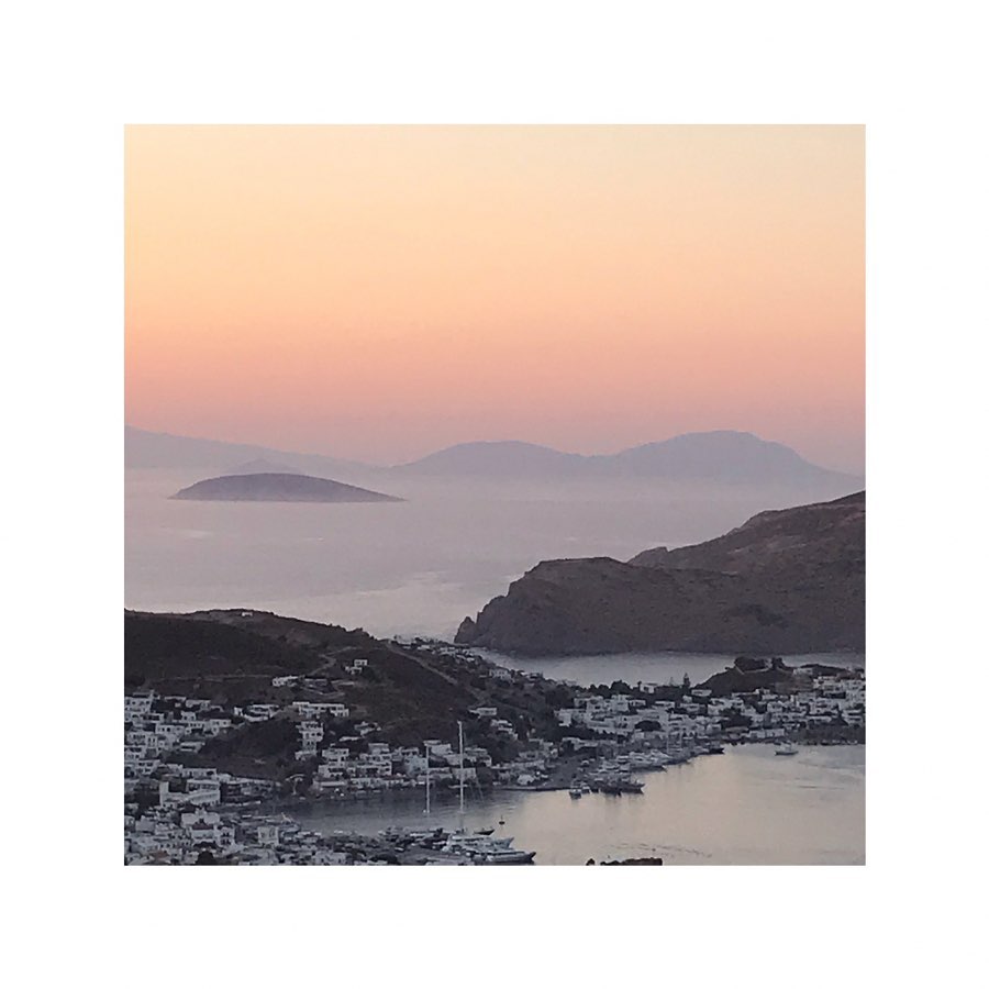 Coastal village landscape at sunset overlooking harbor with boats and hillside architecture, creating a serene and picturesque scene.