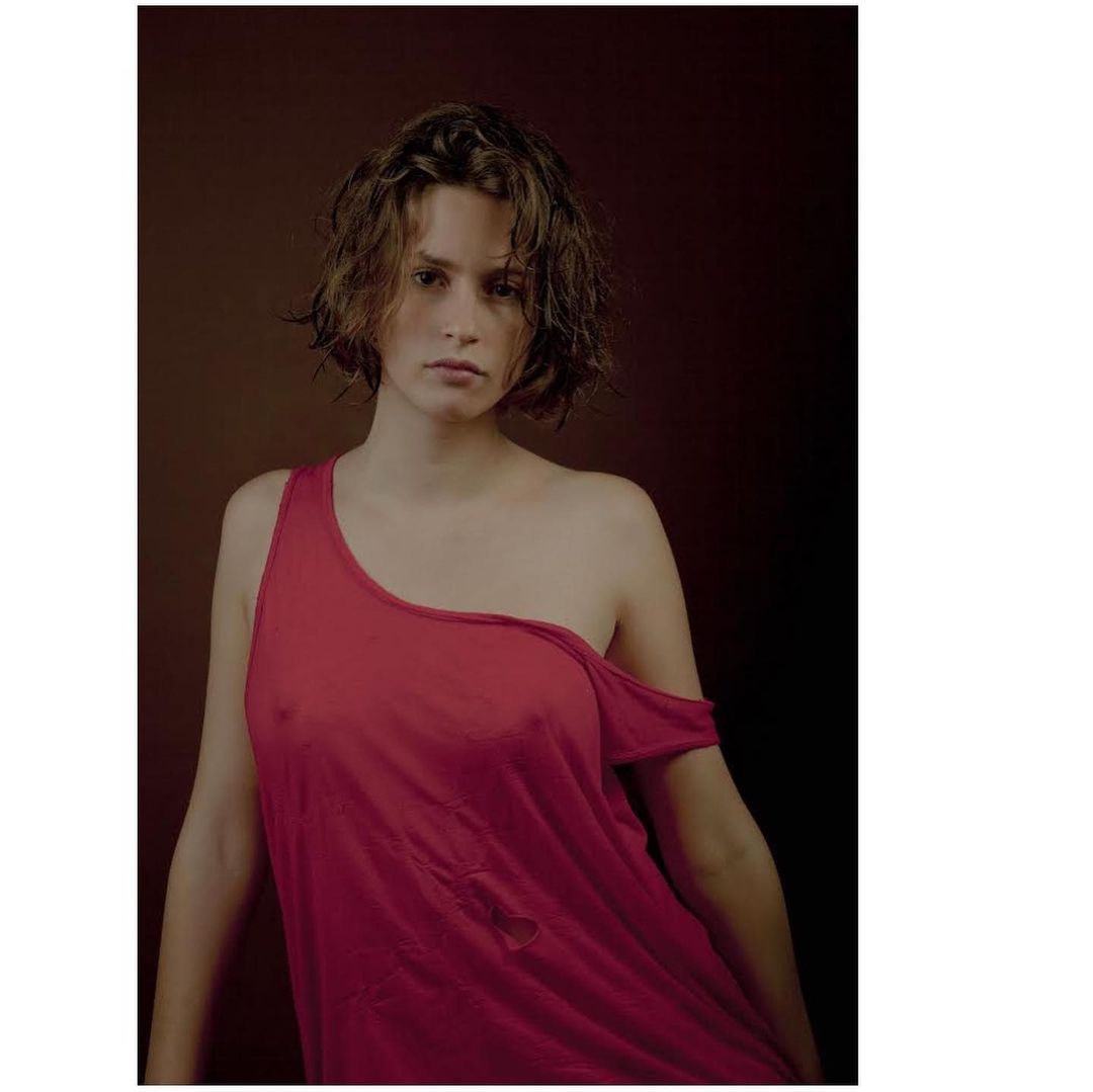 Portrait of a young adult female in a red tank top against a dark brown background, showcasing a simple and intimate studio shot.