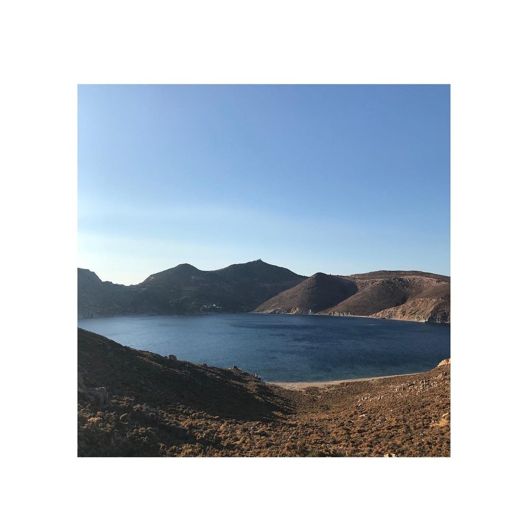 Scenic vista of a tranquil bay surrounded by mountains and hillsides under a clear blue sky, showcasing a peaceful coastal landscape.