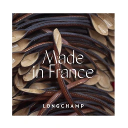Close-up of coiled brown leather bag handles piled together with white text reading Made in France and Longchamp.