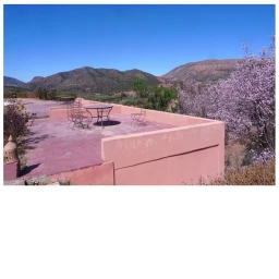 Outdoor rooftop terrace with a round table and wire chairs overlooking distant mountain ranges and blue sky