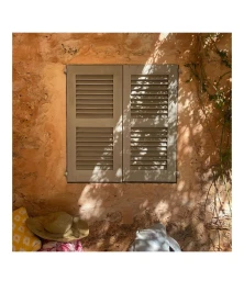 Closed grey louvered shutters set in a textured peach-colored stucco wall with leaf shadows