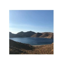 Panoramic view of a deep blue lake nestled between rolling brown hills under a clear sky.