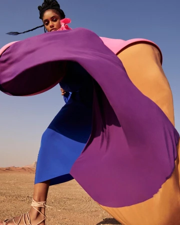 Model wearing a vibrant purple and blue dress with pink accents posing in a desert landscape by Louis Christopher