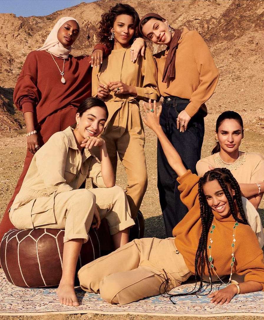 Group of six women of varying skin tones pose outdoors in the desert. They wear diverse, stylish clothing from casual to formal wear.