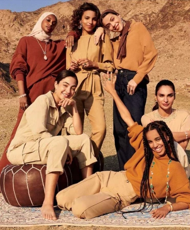 Group of six women of varying skin tones pose outdoors in the desert. They wear diverse, stylish clothing from casual to formal wear.