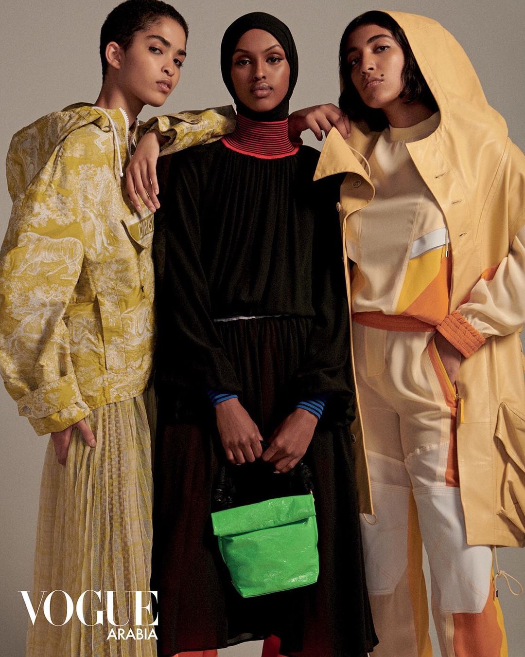 Three fashion models pose in a photo studio, wearing stylish outfits and a hijab, showcasing Vogue Arabia's editorial fashion.